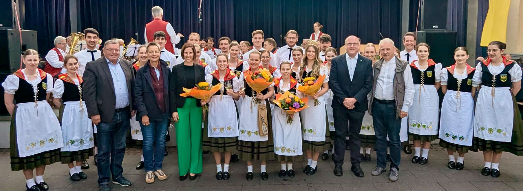 Gruppenbild Gruppenbild mit Trachtengruppe und weiteren Personen vor einer Bühne