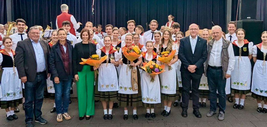 Gruppenbild mit Trachtengruppe und weiteren Personen vor einer Bühne