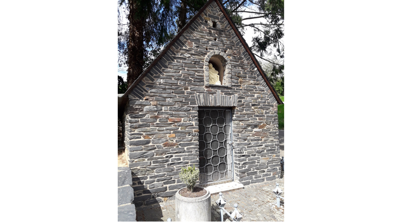 Zu sehen ist die Eingangsseite der Kapelle in der Goldkuppstraße in Mehring. Die Fassade ist aus Schiefersteinen erstellt.