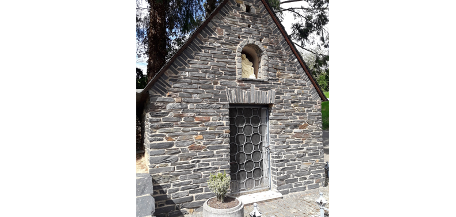Zu sehen ist die Eingangsseite der Kapelle in der Goldkuppstraße in Mehring. Die Fassade ist aus Schiefersteinen erstellt.