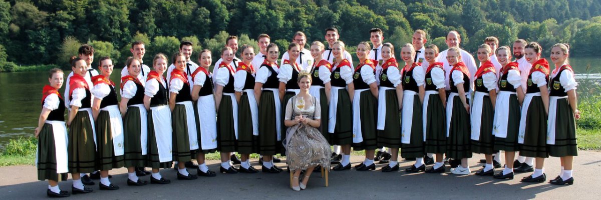 Winzertanzgruppe Mehring und Weinkönigin Laura I Bild zeigt die Weinkönigin Laura I sitzend. Dahinter die Winzertanzgruppe Mehring